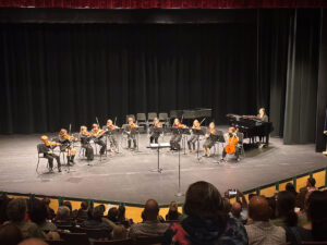 elementary students playing stringed instruments on stage