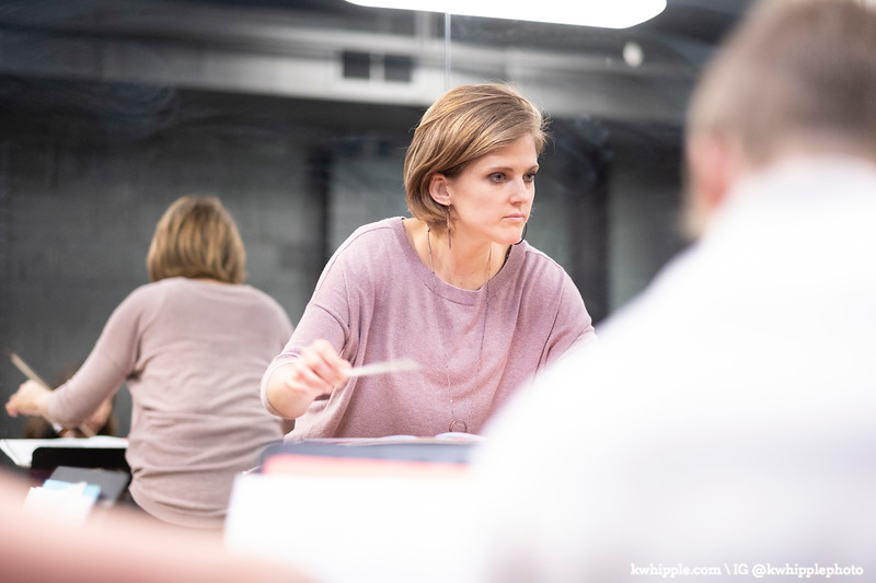 action photo showing Julie Stoessel, CWS alum, conducting with a mirrored reflection behind her