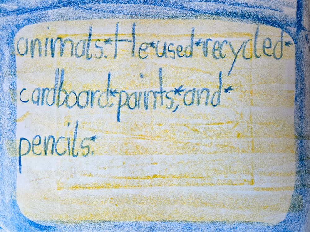 First grade student writing about artist Bill Traylor in large crayon letters on paper